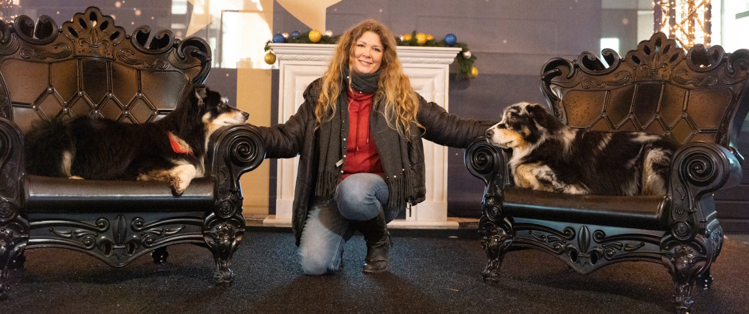 Inhaberin der Hundeschule Balanced Dogwork knieend zwischen ihren beiden Hunden, die links und rechts von ihr auf einem Stuhl liegen